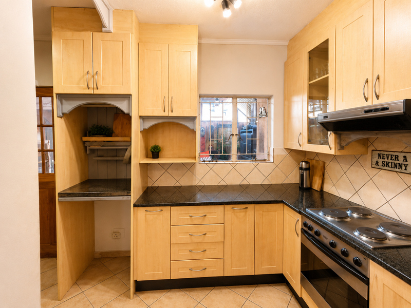 A functional kitchen featuring light wood cabinetry, granite countertops, a built-in oven with electric hob, and a tiled backsplash.
