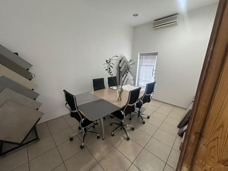 A functional office space featuring tiled flooring, a wall-mounted air conditioning unit, and natural light from a window with fitted blinds.
