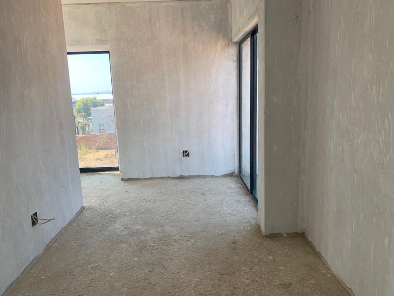 An unfinished bedroom interior featuring plastered walls, concrete flooring, and large aluminium sliding doors providing natural light and outdoor access.