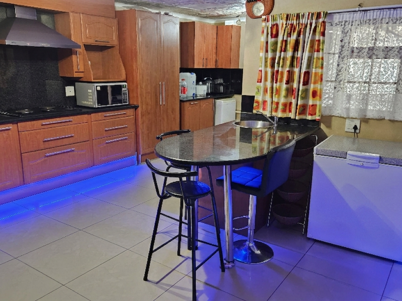 A kitchen featuring wooden cabinetry, granite countertops, built-in oven, and a breakfast bar, accented with blue LED strip lighting and tiled flooring.