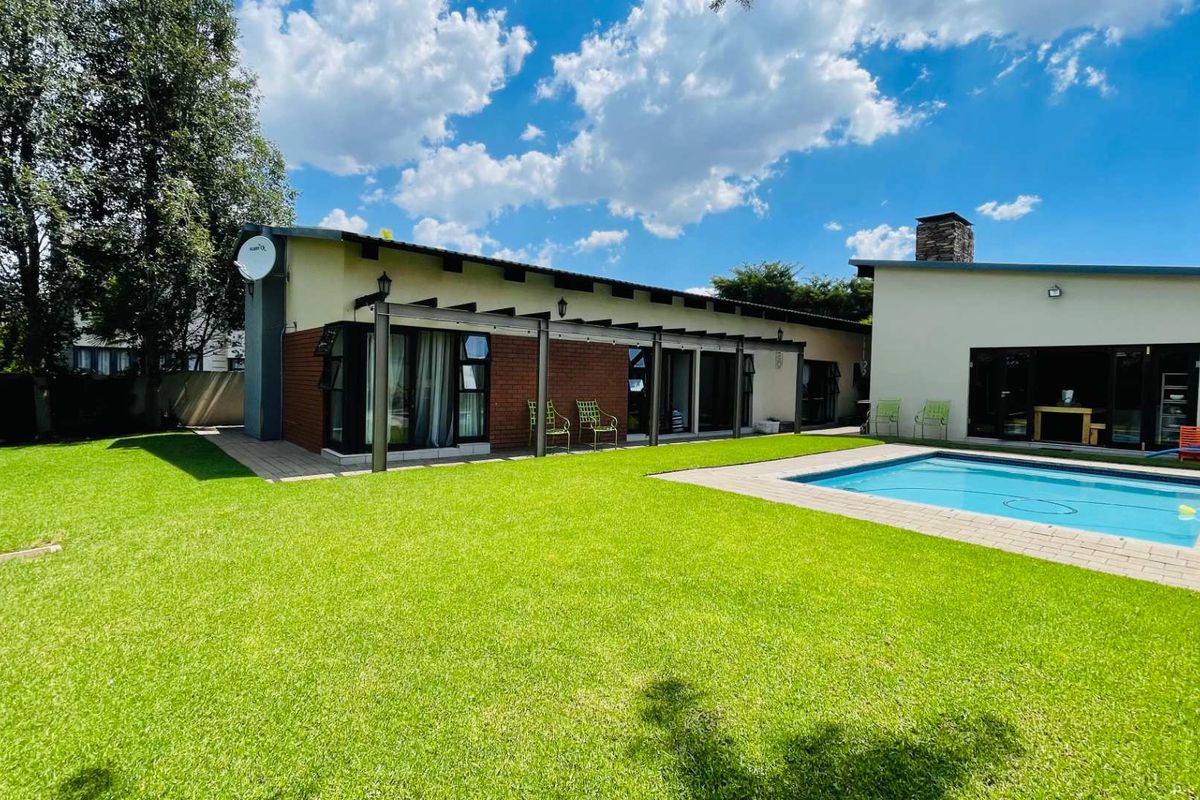 Spacious rear garden featuring a well-maintained lawn, a swimming pool with paved surround, and a covered patio area attached to the main house.