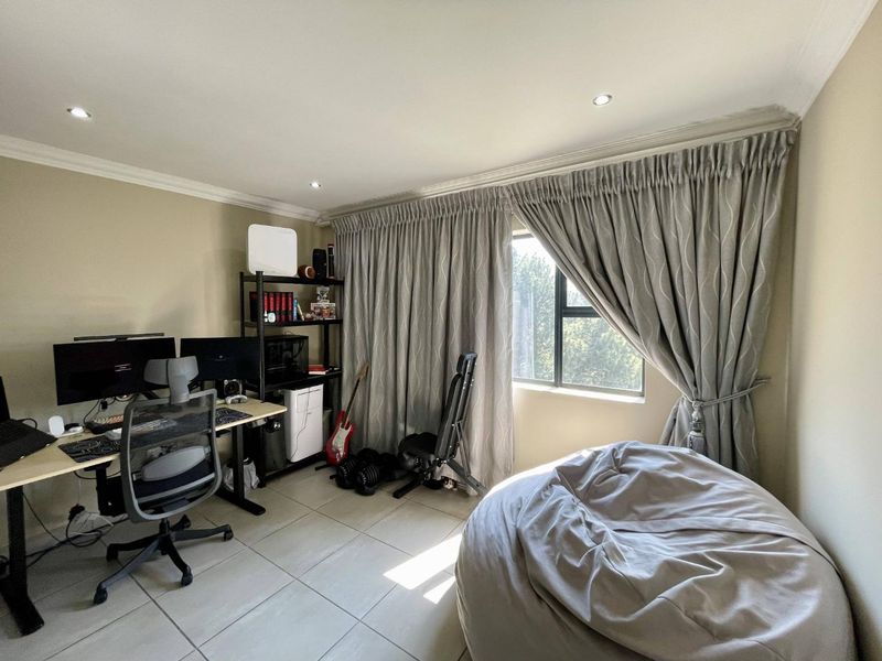 A functional home office space featuring tiled flooring, recessed downlighting, and large windows with floor-to-ceiling curtains.