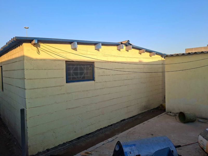 Rear exterior view of the property showing a concrete block structure with a corrugated metal roof and exposed rafters.