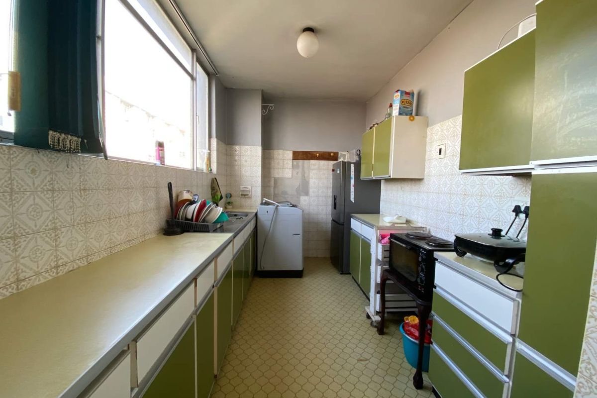 A dated galley-style kitchen featuring original cabinetry, tiled backsplash, and vinyl flooring, offering significant potential for a modern renovation.