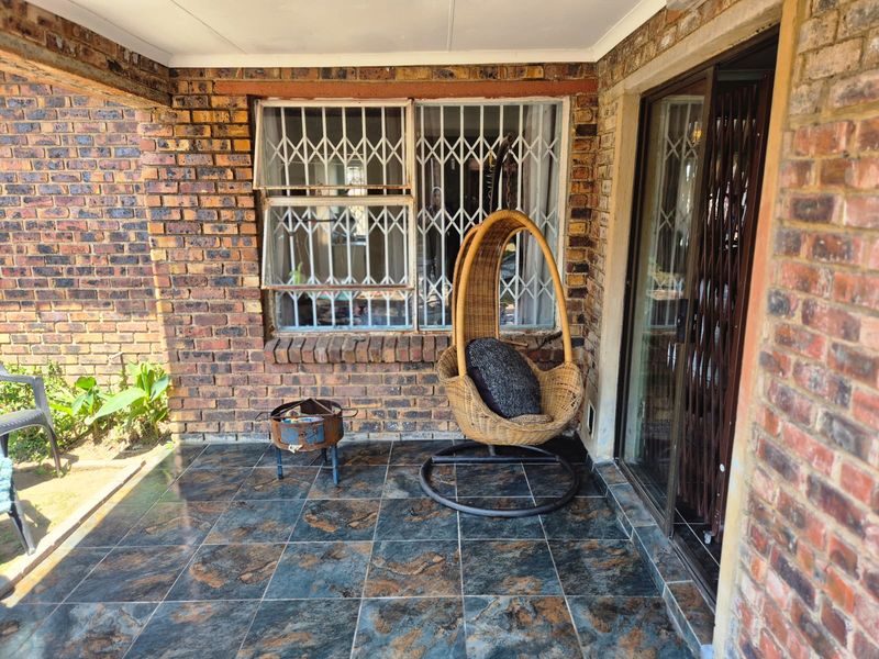 A covered patio area featuring exposed brick walls, dark tiled flooring, and sliding glass doors with security gates.