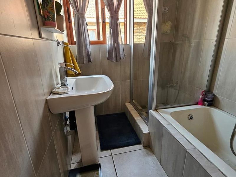 A functional bathroom featuring a pedestal basin, a combined shower and bathtub enclosure, and neutral floor-to-ceiling tiling.