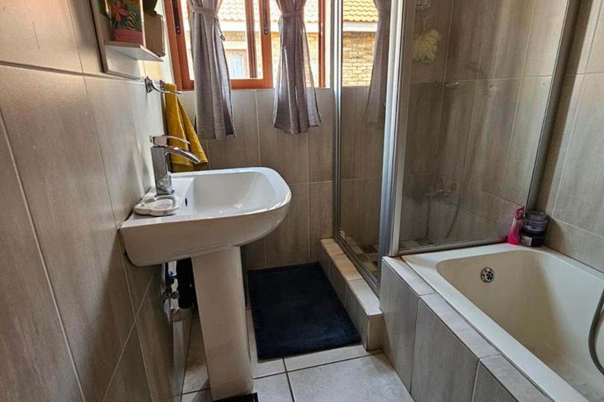 A functional bathroom featuring a pedestal basin, a combined shower and bathtub enclosure, and neutral floor-to-ceiling tiling.