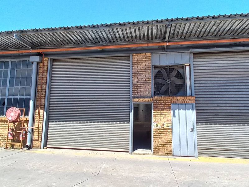 Industrial warehouse exterior featuring multiple roller shutter doors, brick facade, and integrated ventilation fan, set on a concrete apron.