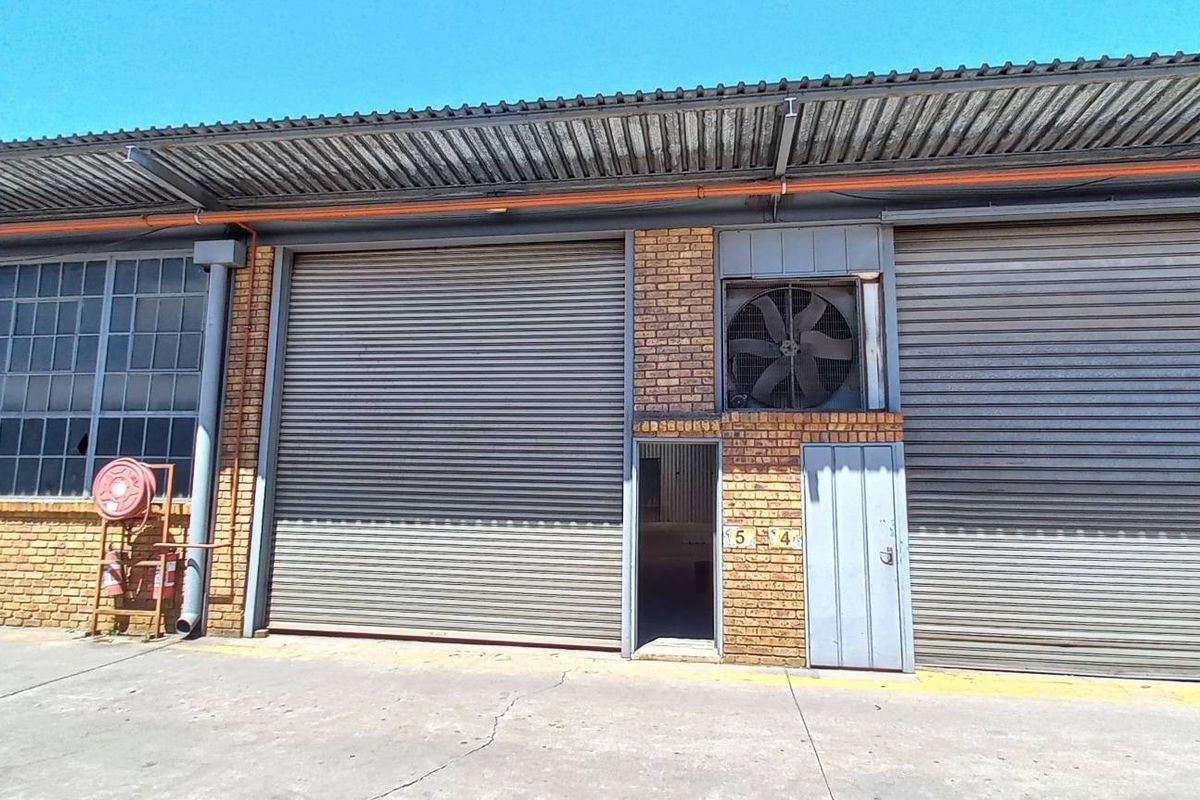 Industrial warehouse exterior featuring multiple roller shutter doors, brick facade, and integrated ventilation fan, set on a concrete apron.
