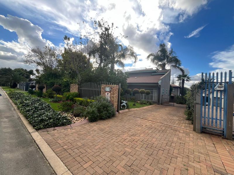 Front view of the property featuring a brick paved driveway, secure metal gate, and established garden landscaping.
