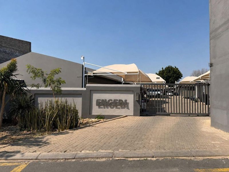 Front entrance view of the apartment complex featuring a paved driveway, secure sliding gate, and covered shade sail parking bays.