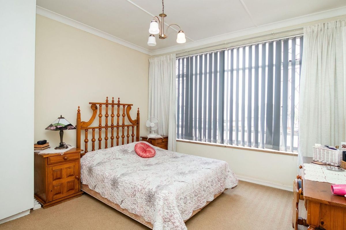 A well-lit bedroom featuring built-in cupboards, neutral carpeting, and large windows with vertical blinds, offering a comfortable and functional living space.