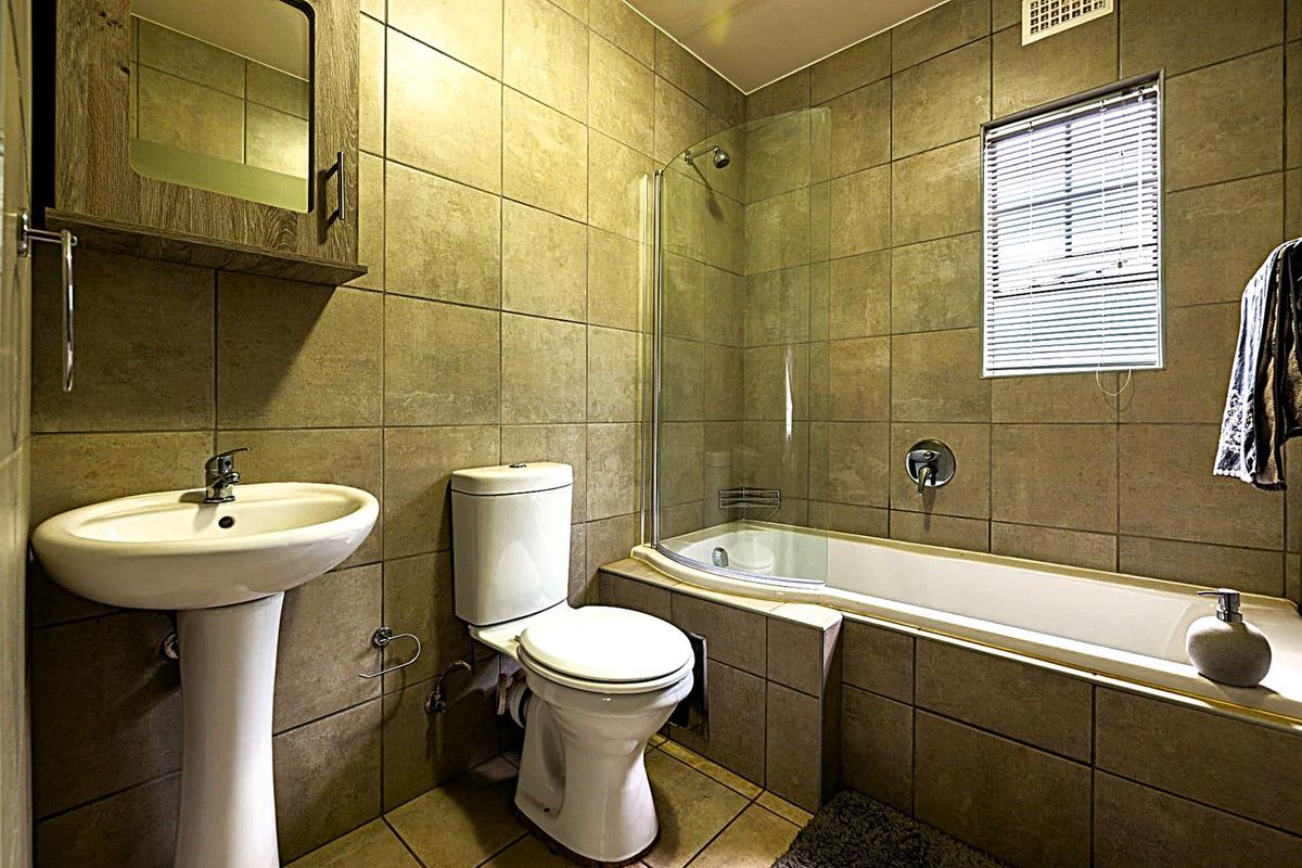 A functional bathroom featuring full-height wall tiling, a pedestal basin, a toilet, and a bathtub with a glass shower screen.