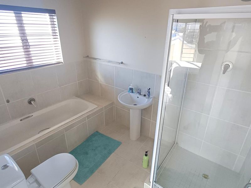 A functional bathroom featuring a separate shower enclosure, built-in bathtub, pedestal basin, and toilet with neutral wall tiling.