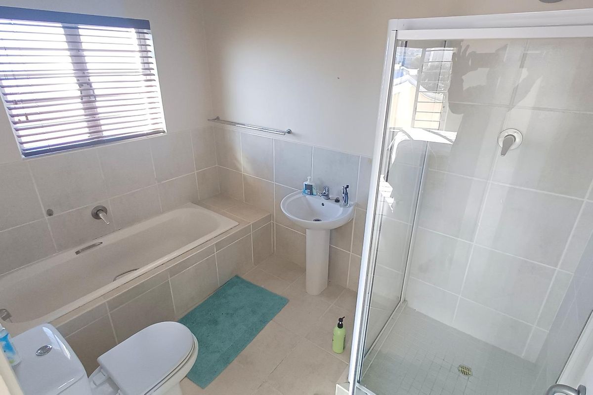 A functional bathroom featuring a separate shower enclosure, built-in bathtub, pedestal basin, and toilet with neutral wall tiling.