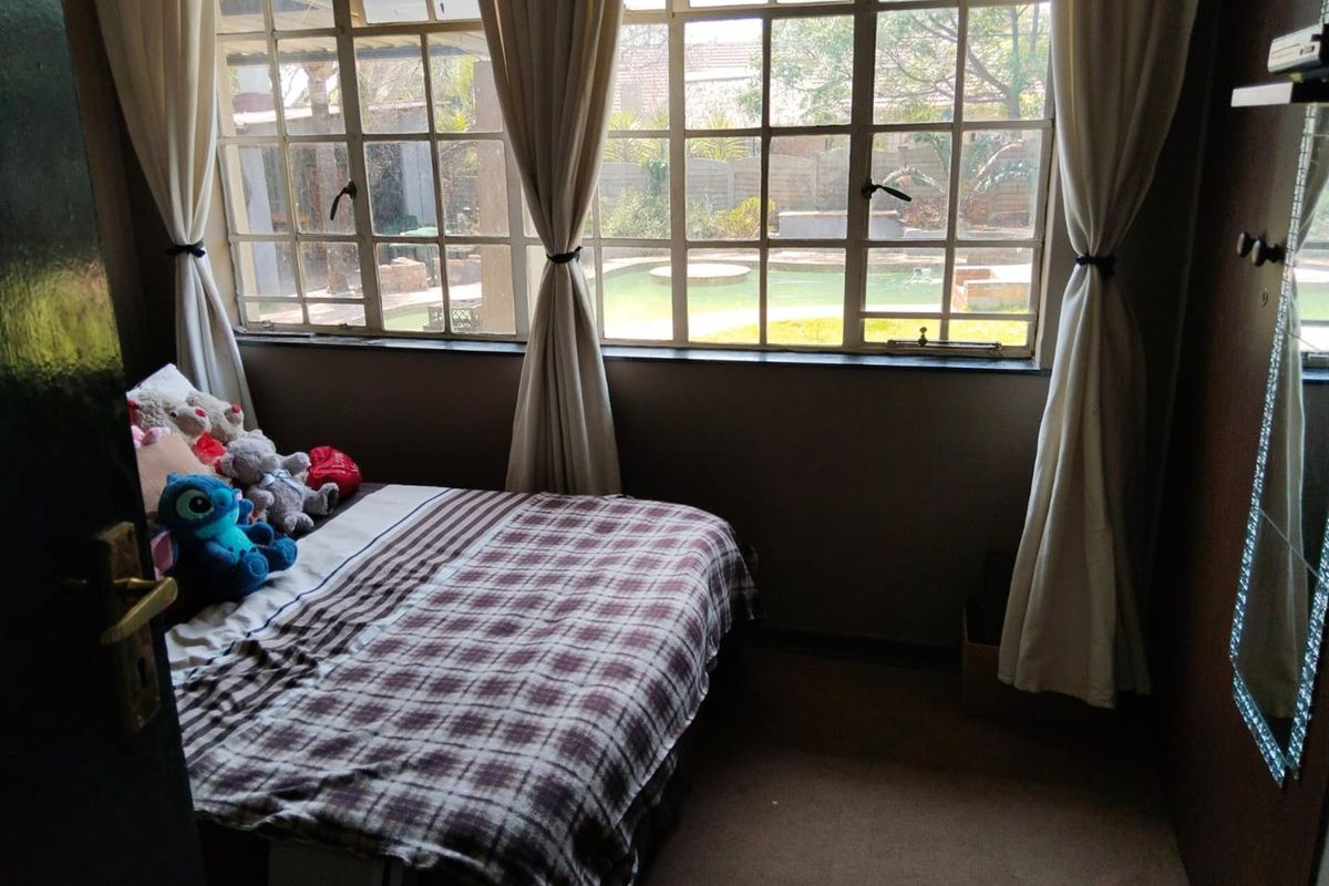 A bedroom featuring large grid-style windows with views overlooking the backyard pool area.