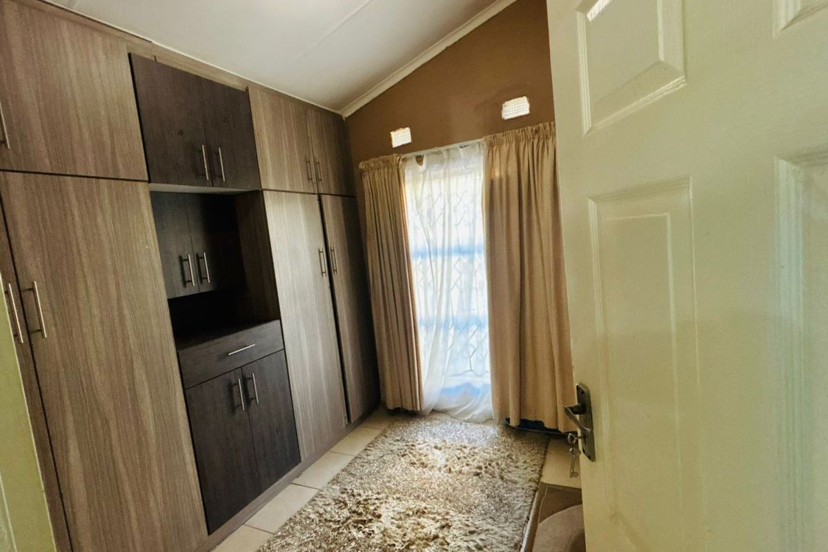 A bedroom featuring built-in wooden cabinetry with integrated shelving and storage, tiled flooring, and a window with curtain treatments.