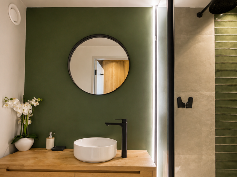 Modern bathroom featuring a vessel sink on a wooden vanity, a walk-in shower with green accent tiles, and stylish black fixtures.