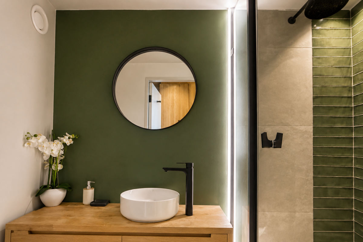 Modern bathroom featuring a vessel sink on a wooden vanity, a walk-in shower with green accent tiles, and stylish black fixtures.