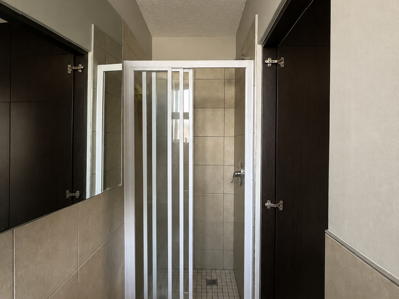 A functional bathroom featuring a shower enclosure, wall-mounted basin with mixer tap, and neutral wall tiling.