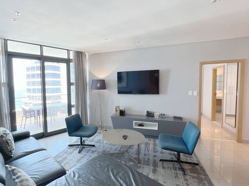 A bright and modern living room featuring tiled floors, recessed lighting, and large sliding glass doors providing access to the balcony.