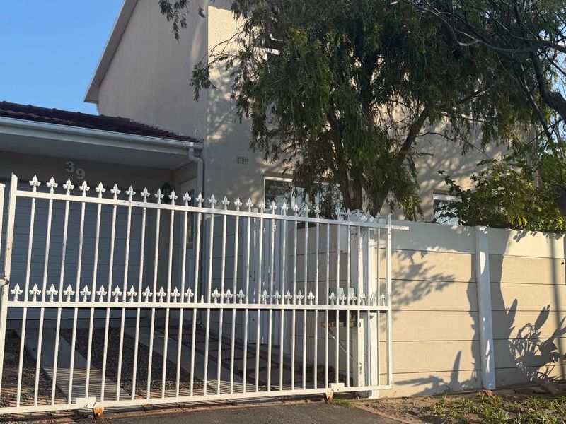 Front elevation of the property featuring a white metal security gate, precast boundary wall, and plastered exterior facade.