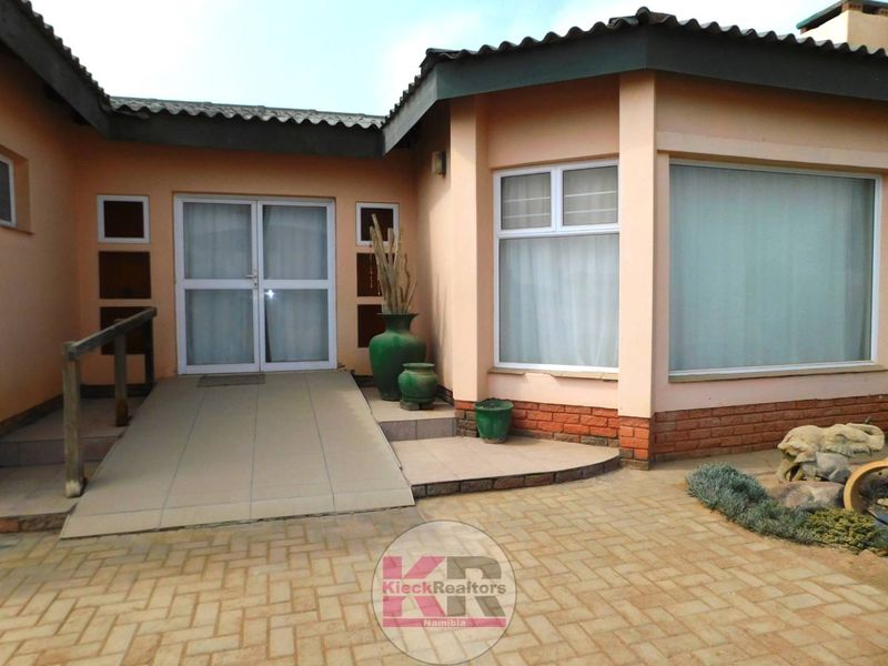 Rear exterior view of the property featuring a tiled access ramp, brick paving, and large windows with sliding glass door access.