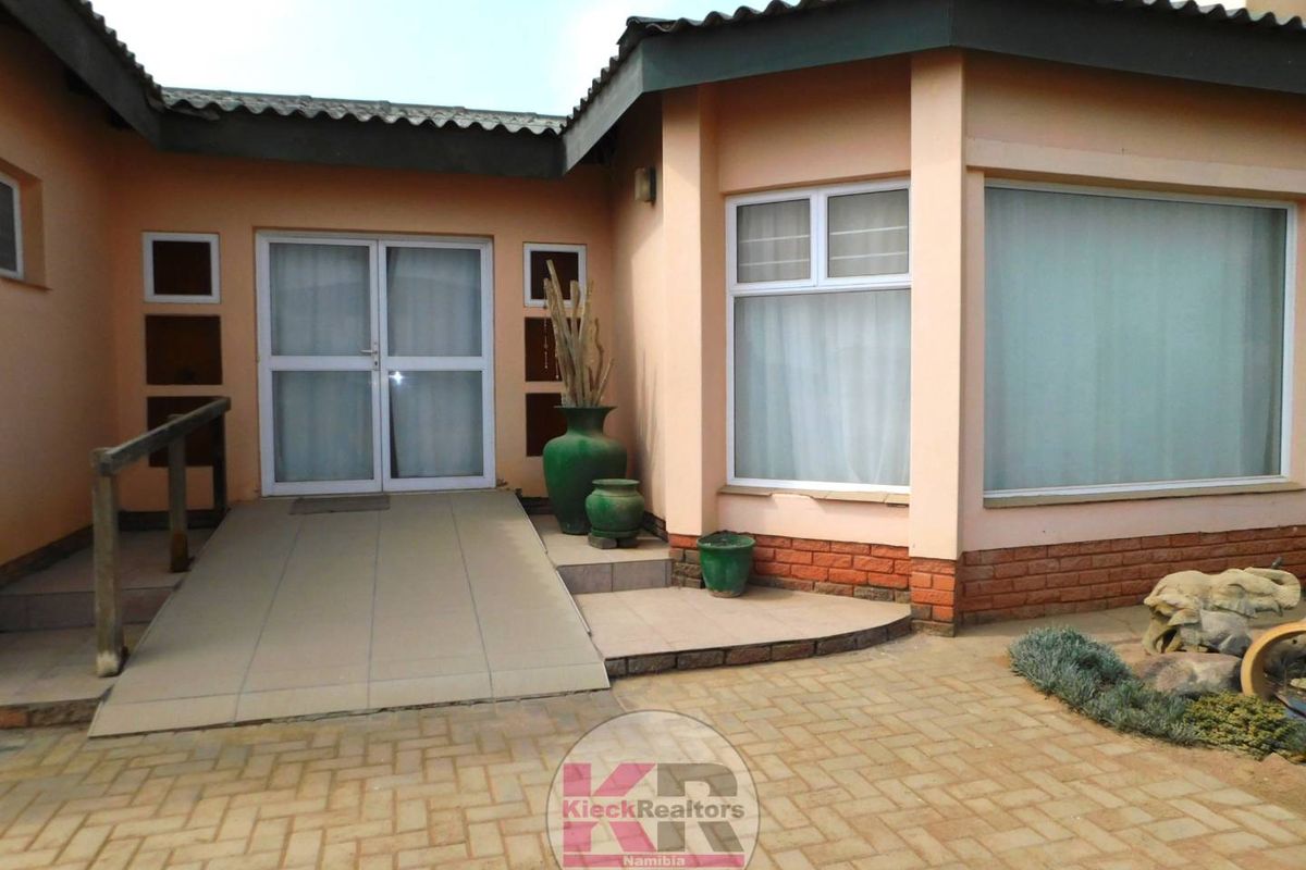 Rear exterior view of the property featuring a tiled access ramp, brick paving, and large windows with sliding glass door access.