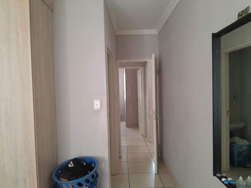 A functional hallway featuring tiled flooring, coving, and built-in cupboard storage, providing access to adjacent rooms within the apartment.