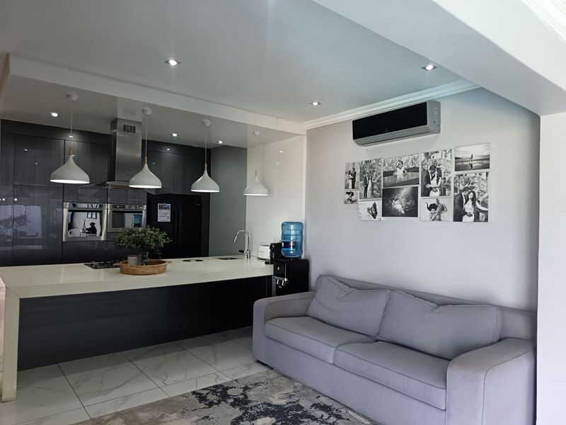 Modern open-plan kitchen and living area featuring dark cabinetry, a central island with integrated appliances, and sleek tiled flooring.
