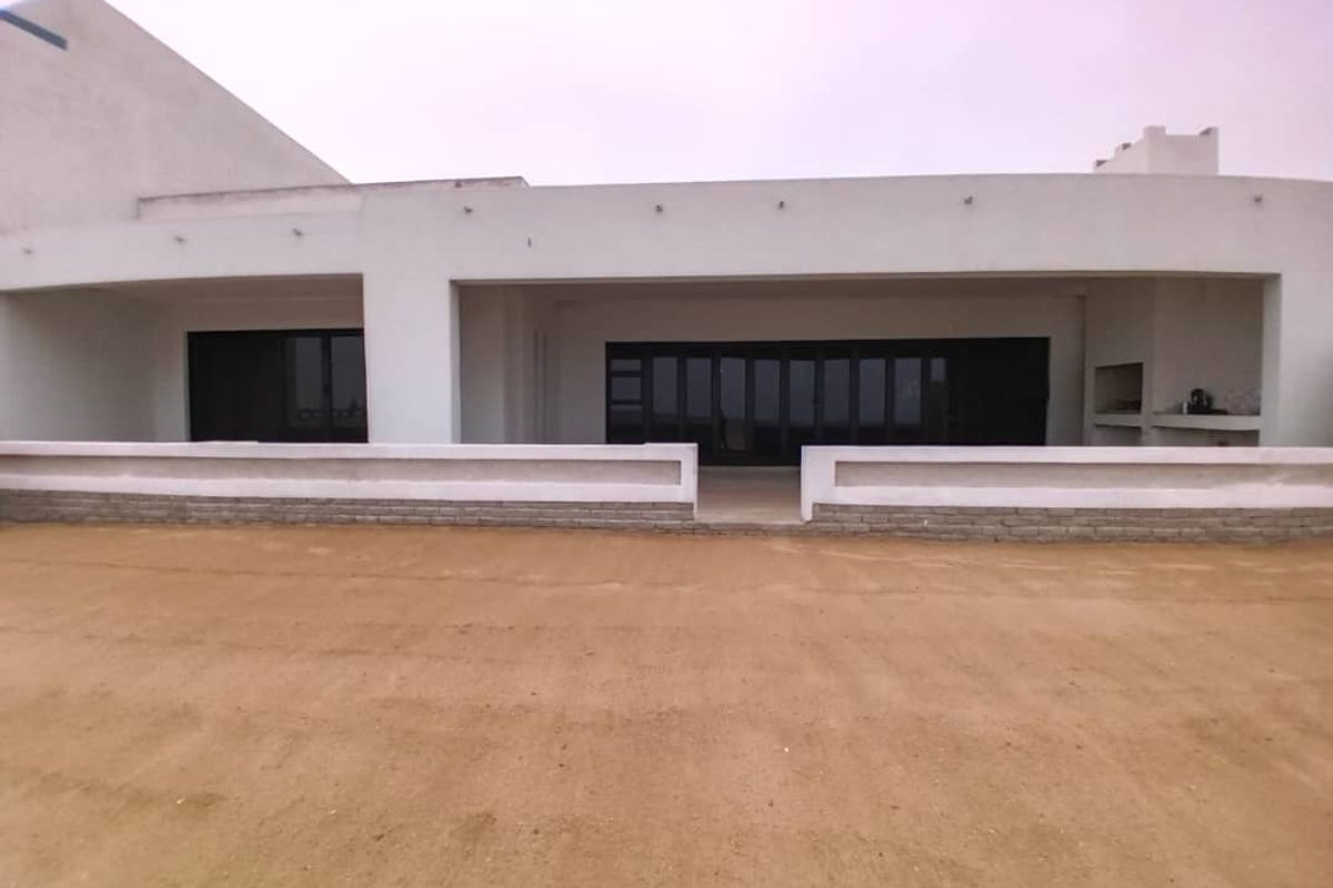 Rear view of a modern home featuring a covered patio with a built-in braai and large sliding glass doors, overlooking an unfinished garden area.