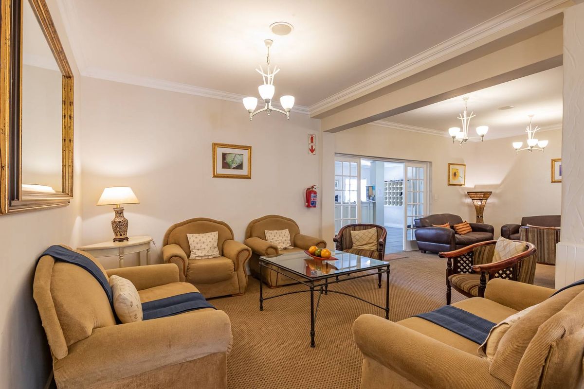A spacious, carpeted living area featuring crown molding, multiple chandeliers, and French doors leading to an adjacent room.
