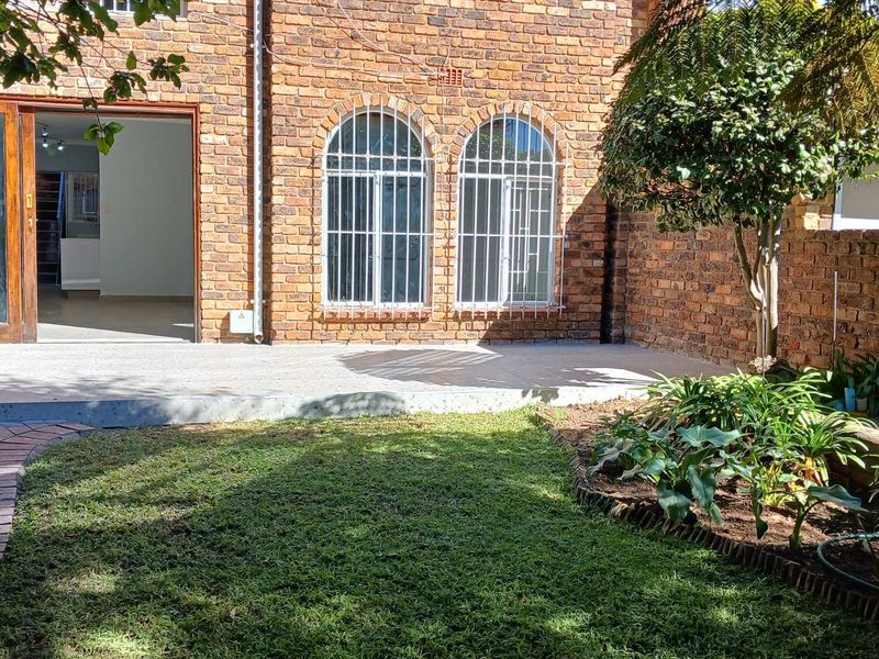 A private rear garden featuring a paved patio area, face brick exterior walls, and arched windows with security bars.