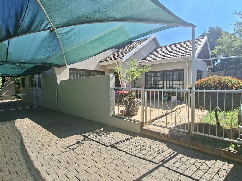 Front exterior view featuring a paved driveway, a shade cloth carport, and a secure gated entrance to the property.