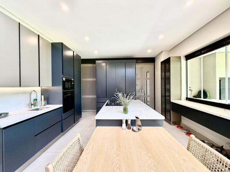 Modern kitchen featuring dark cabinetry, stone countertops, a central island with a gas hob, and integrated appliances in a sleek, contemporary design.