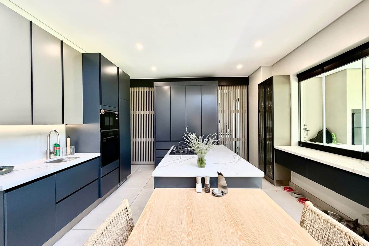 Modern kitchen featuring dark cabinetry, stone countertops, a central island with a gas hob, and integrated appliances in a sleek, contemporary design.