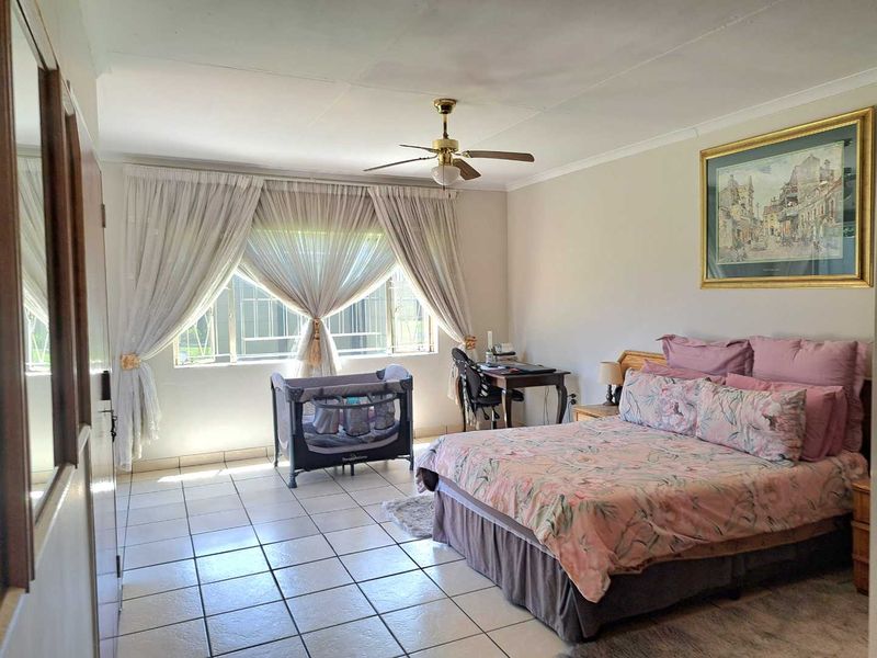 A spacious bedroom featuring tiled flooring, a ceiling fan, and large windows with security bars, offering a functional and well-lit living space.