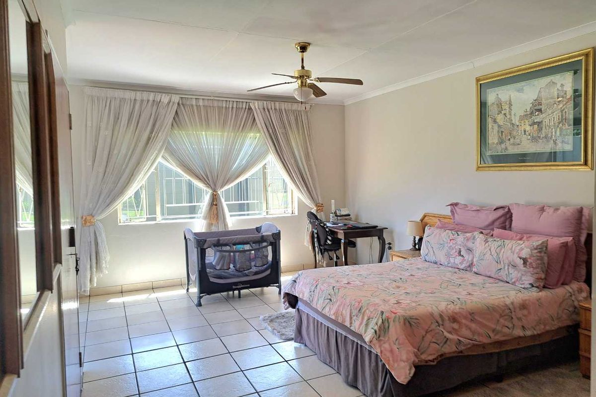 A spacious bedroom featuring tiled flooring, a ceiling fan, and large windows with security bars, offering a functional and well-lit living space.
