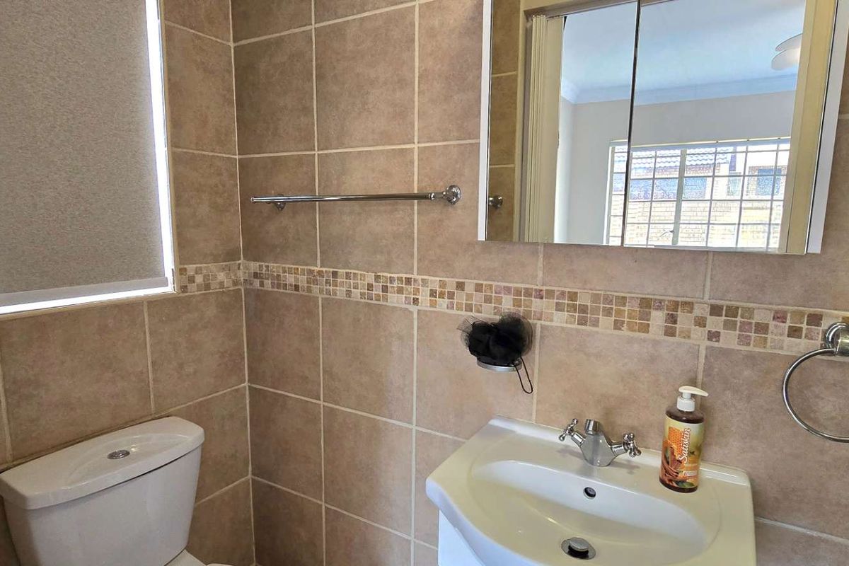 A functional bathroom featuring tiled walls with a decorative mosaic border, a wall-mounted vanity basin, a toilet, and a mirrored medicine cabinet.