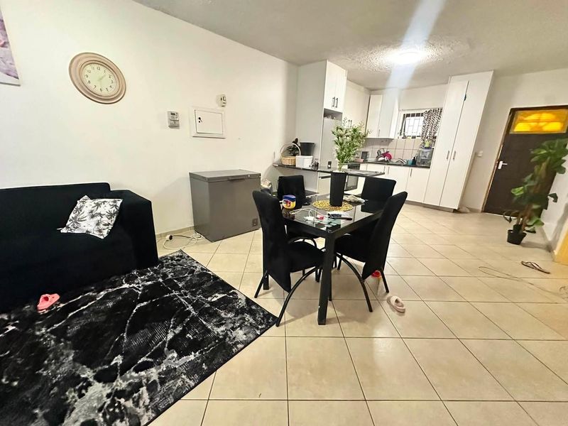 Open-plan living and dining area featuring tiled flooring and a functional kitchen with built-in cabinetry and integrated appliances.