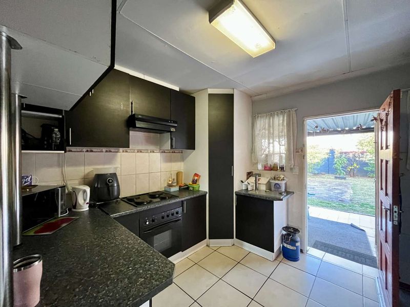 A functional kitchen featuring dark cabinetry, laminate countertops, built-in oven and hob, tiled flooring, and direct access to the rear garden area.