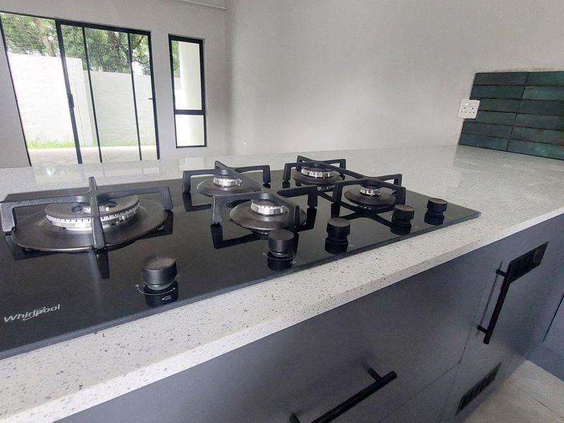 Modern kitchen featuring a sleek black gas hob, quartz countertops, and dark cabinetry with a stylish tiled splashback.