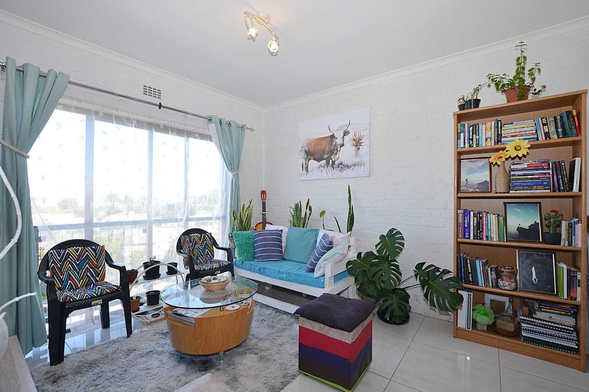 A bright living room featuring tiled flooring, a large sliding glass door providing natural light, and a textured painted brick wall.