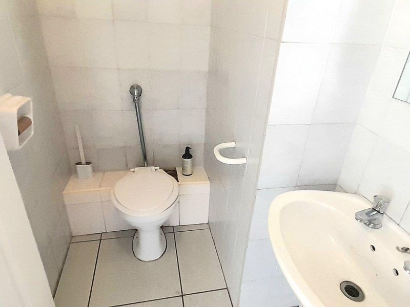A functional bathroom featuring a white ceramic toilet, pedestal basin with chrome taps, and full-height wall tiling.