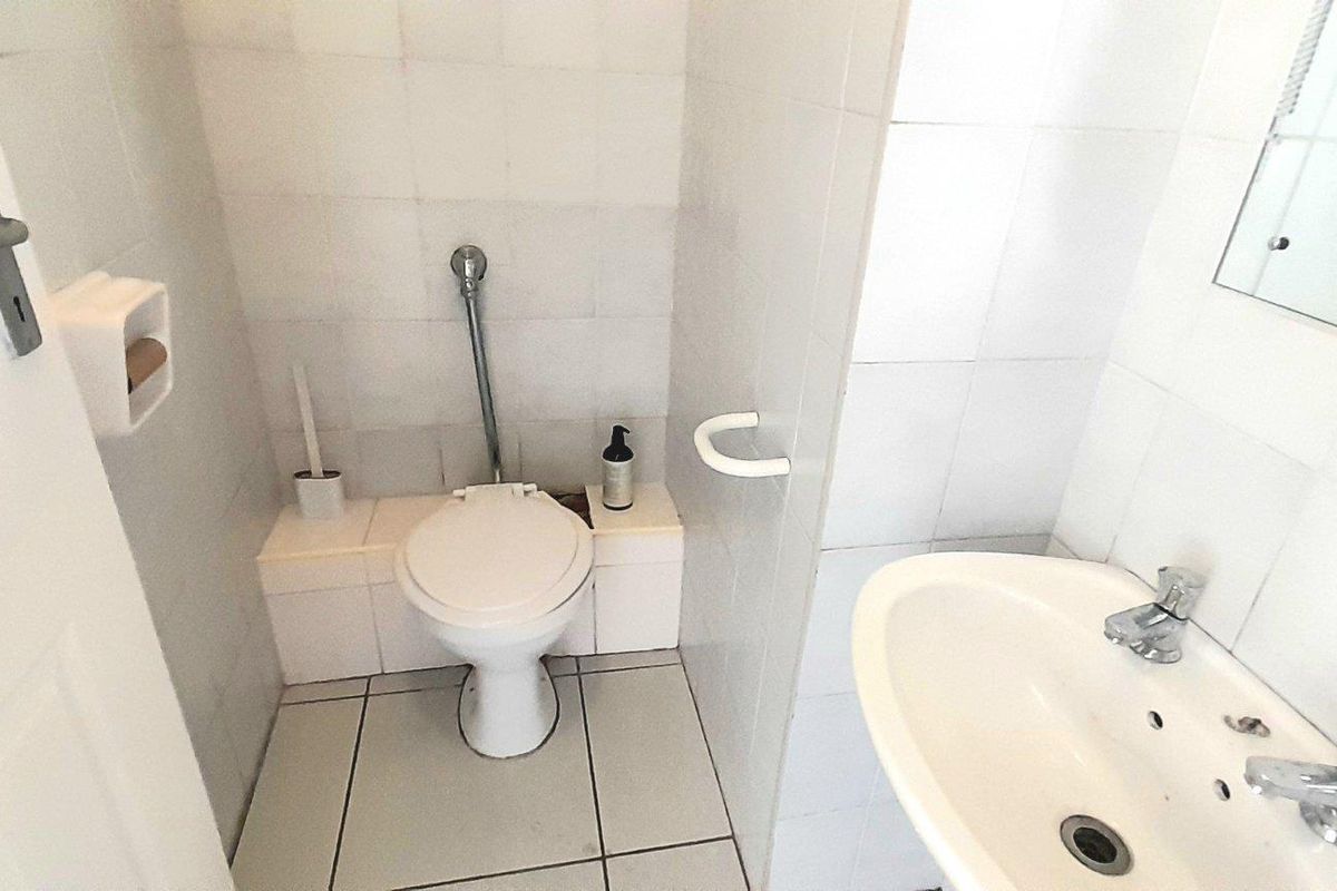 A functional bathroom featuring a white ceramic toilet, pedestal basin with chrome taps, and full-height wall tiling.