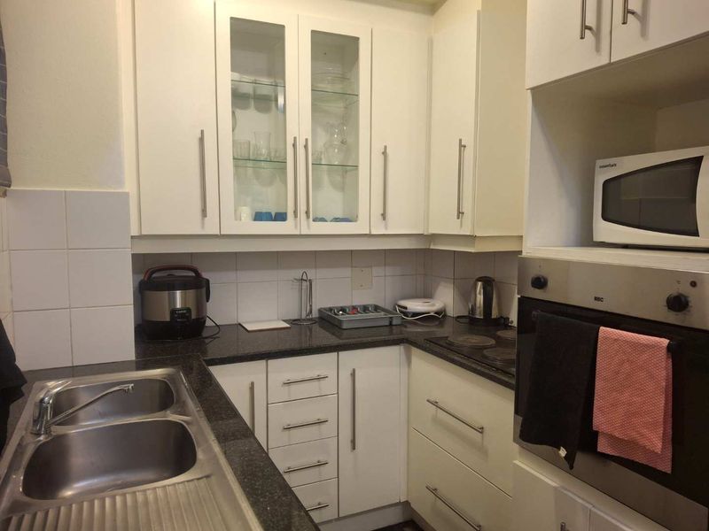 A functional kitchen featuring white cabinetry, granite countertops, a double stainless steel sink, and built-in oven with electric hob.