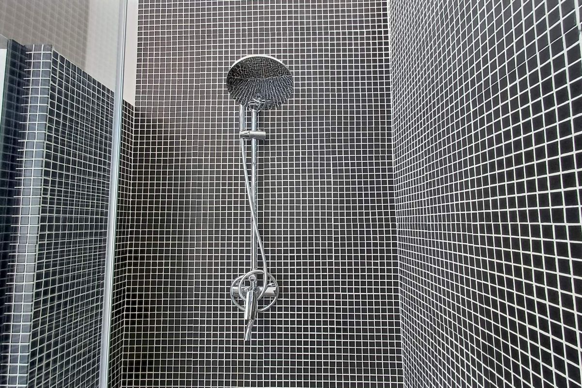A modern shower enclosure featuring sleek black mosaic wall tiles and a contemporary chrome shower fixture.