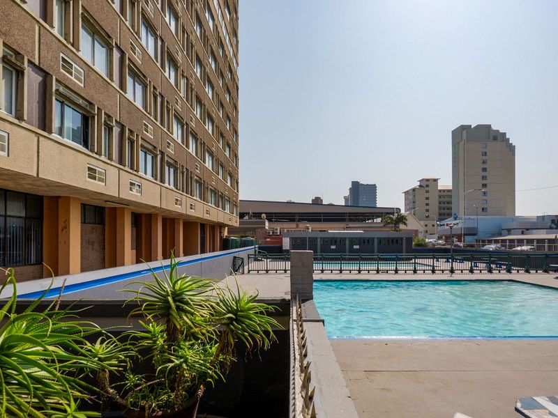 Outdoor swimming pool area featuring a concrete deck and metal perimeter fencing, situated adjacent to a multi-story apartment building.