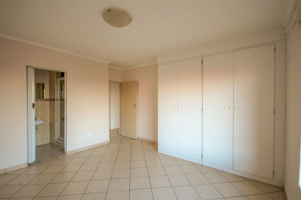A spacious, empty bedroom featuring neutral tiled flooring, built-in cupboards, and direct access to an en-suite bathroom.