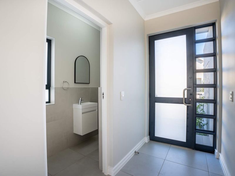 Modern entrance hall featuring a sleek frosted glass front door, neutral tiled flooring, and access to a contemporary guest cloakroom with a wall-mounted vanity.